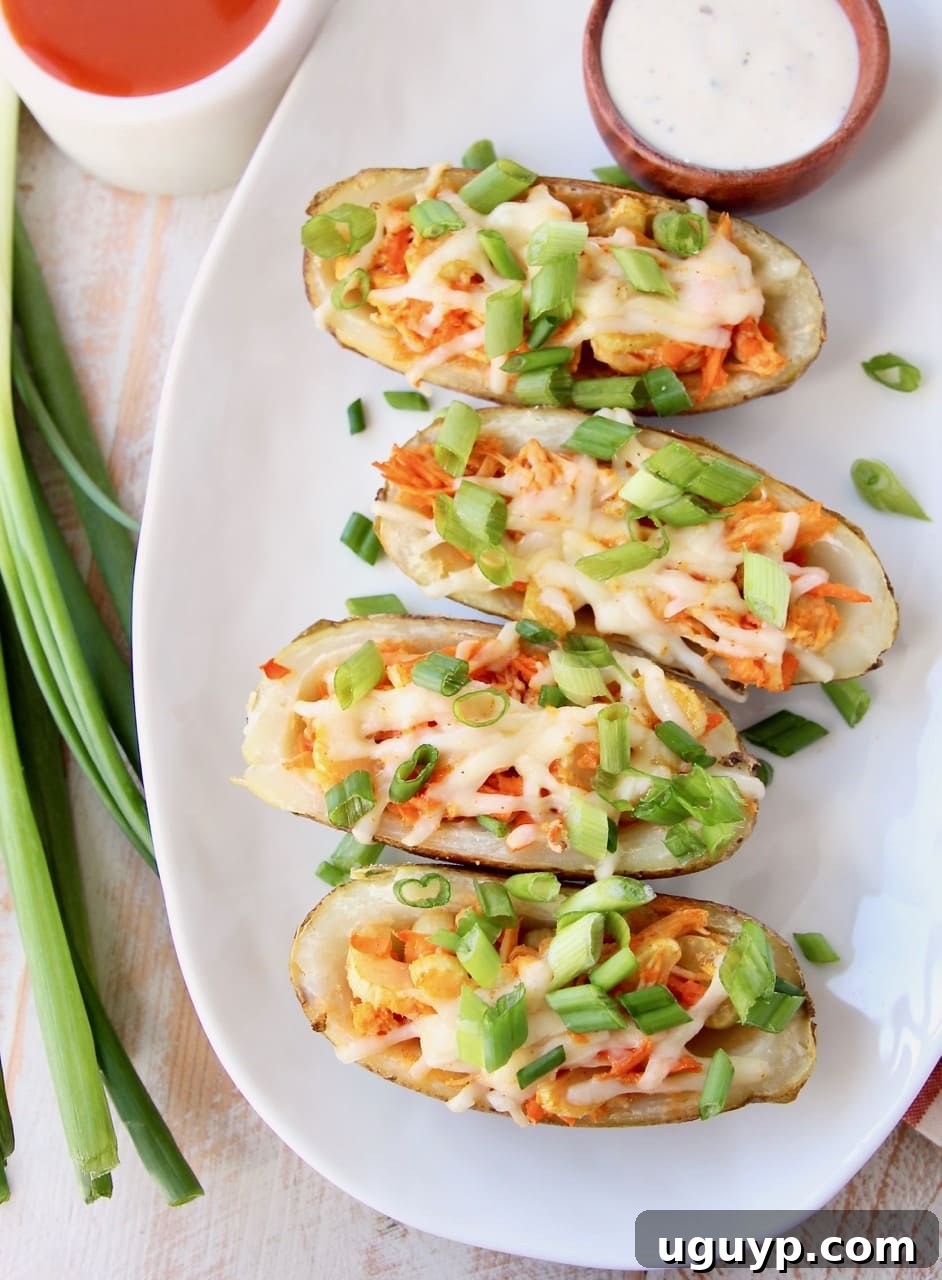 Overhead shot of buffalo chicken potato skins with green onions, side bowl of ranch dressing and side bowl of buffalo sauce
