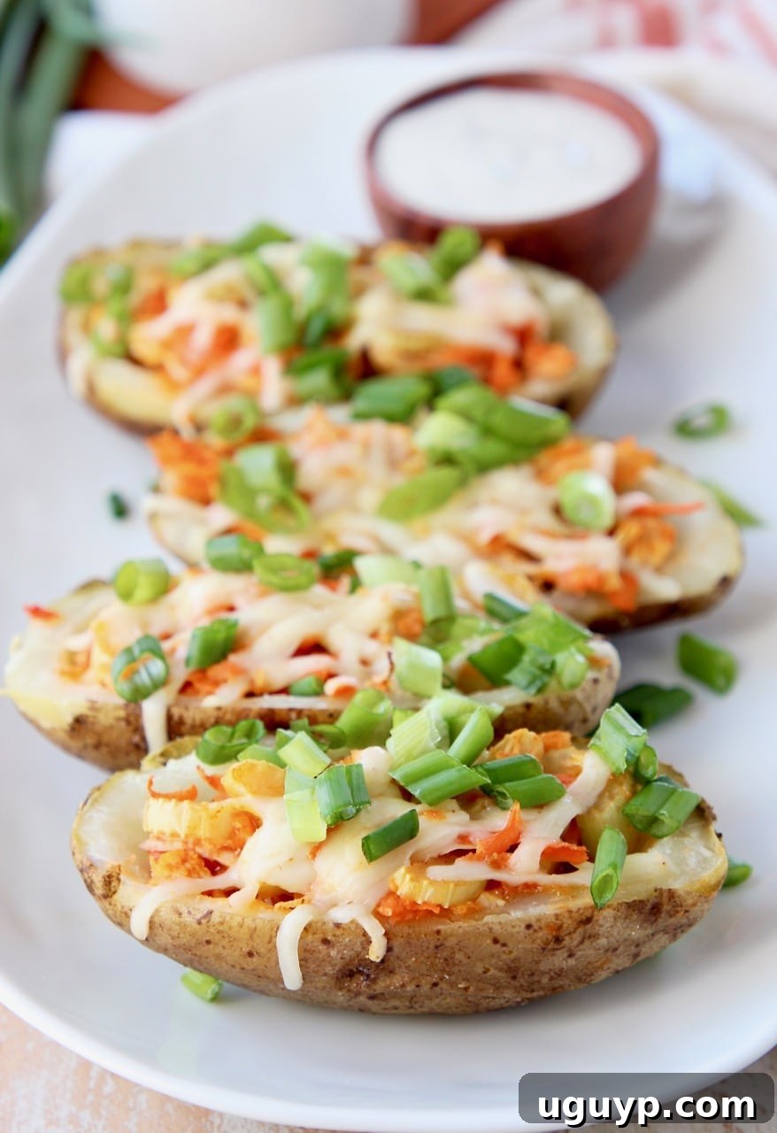 Buffalo Chicken Potato Skins topped with diced green onions on white plate with side ramekin of ranch dressing