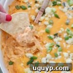 hand lifting chip out of buffalo chicken dip in baking dish