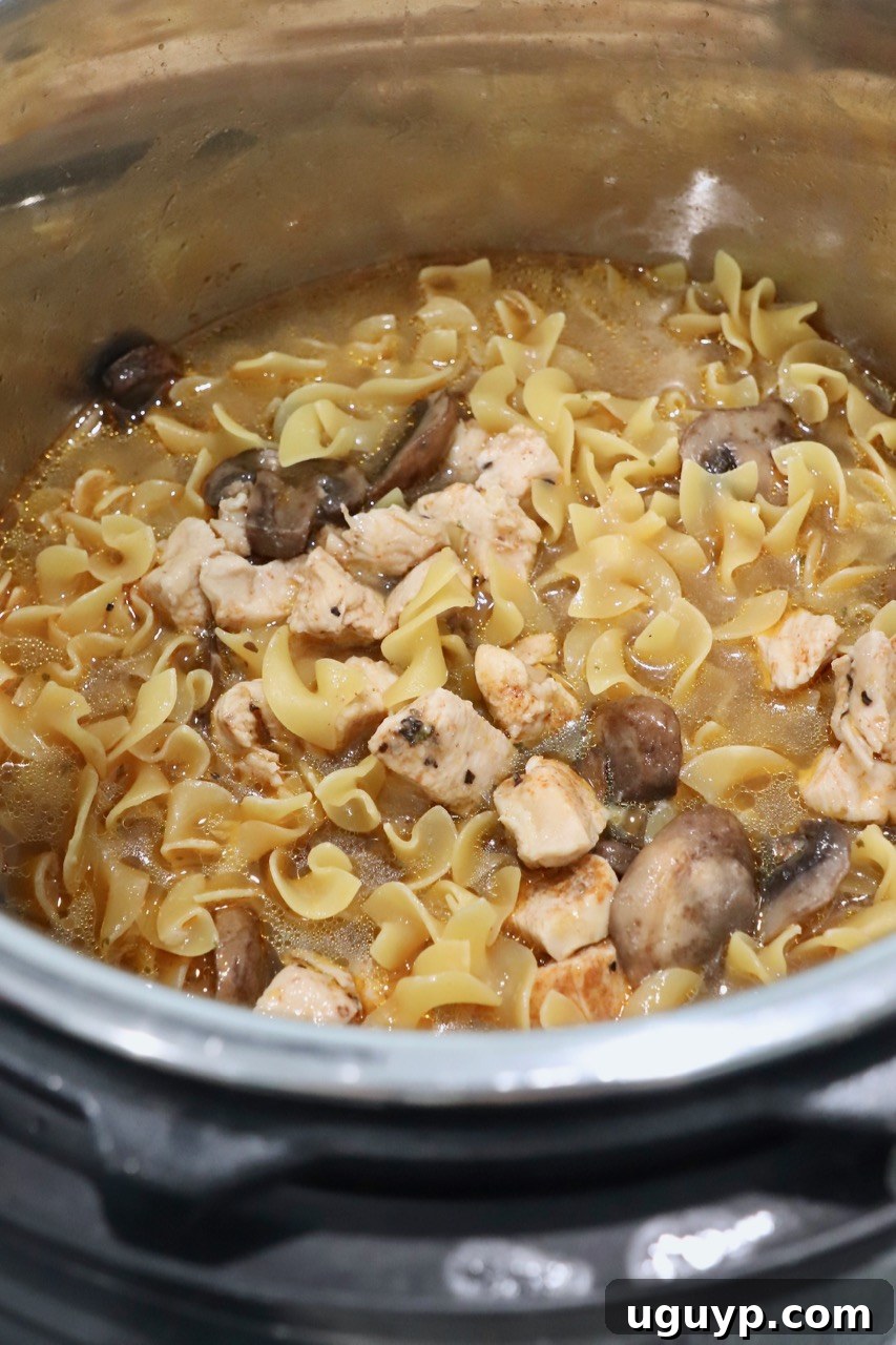 Egg noodles added to the Instant Pot with cooked chicken and vegetables, ready for their cooking cycle.