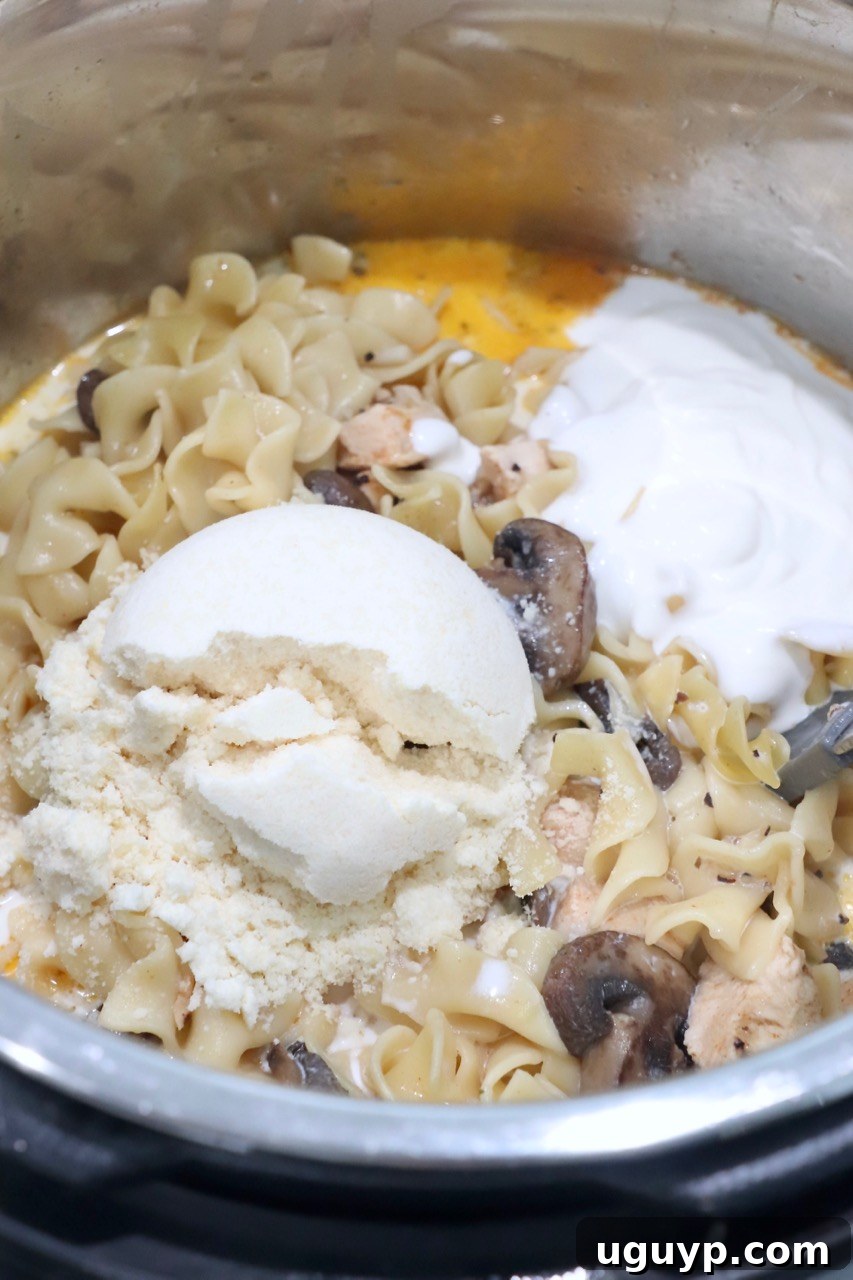 Sour cream, half-and-half, and grated Parmesan cheese being added to the cooked chicken stroganoff in the Instant Pot.