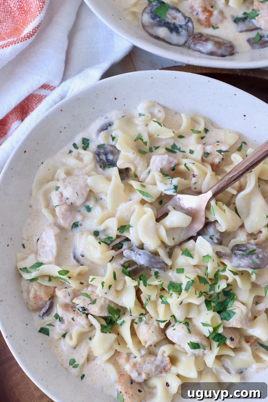 A serving of creamy Instant Pot Chicken Stroganoff in a white bowl with a fork, garnished with fresh parsley.