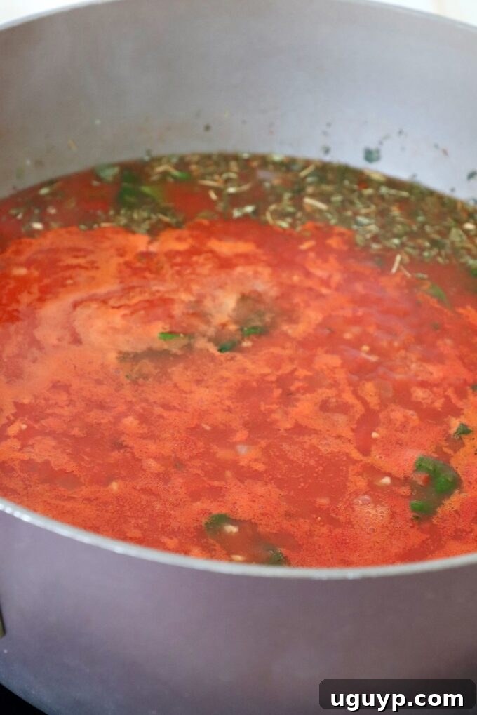 Tomato sauce and Italian seasoning simmering in a large pot on the stove, forming the rich base for the tortellini soup.
