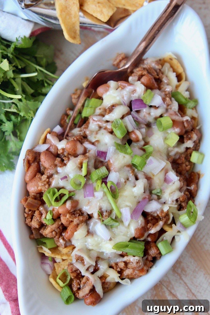 frito chili pie in white oval bowl topped with diced green onions