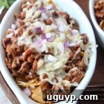 frito chili pie topped with cheese and diced red onion