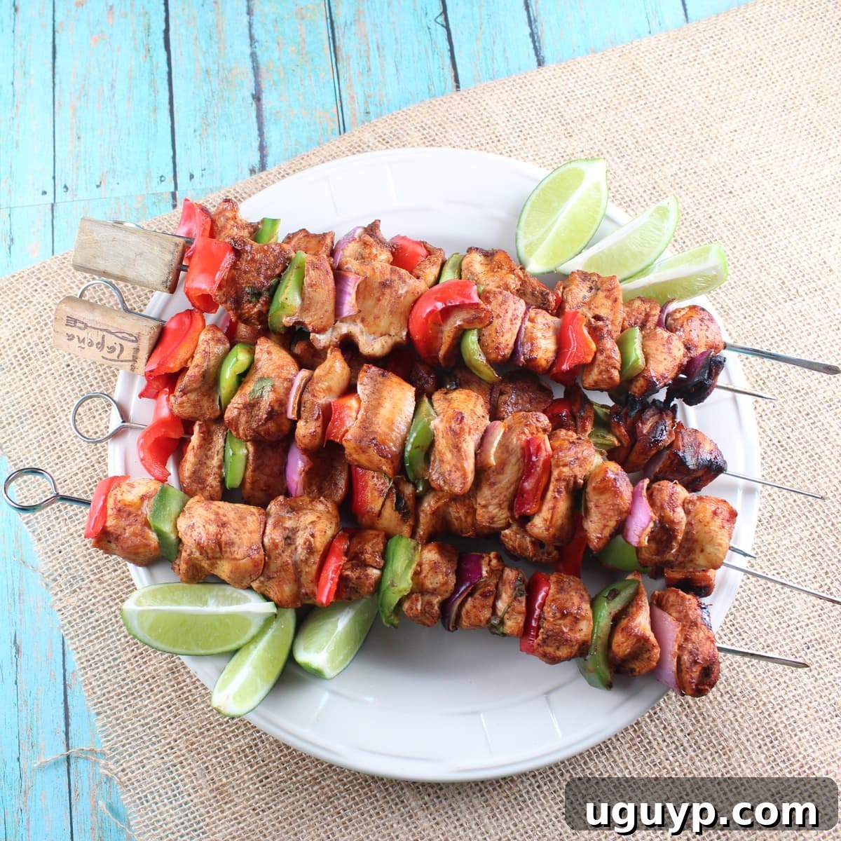 Grilled Chipotle Lime Chicken Fajita Skewers stacked on a white plate, garnished with fresh lime wedges and cilantro.