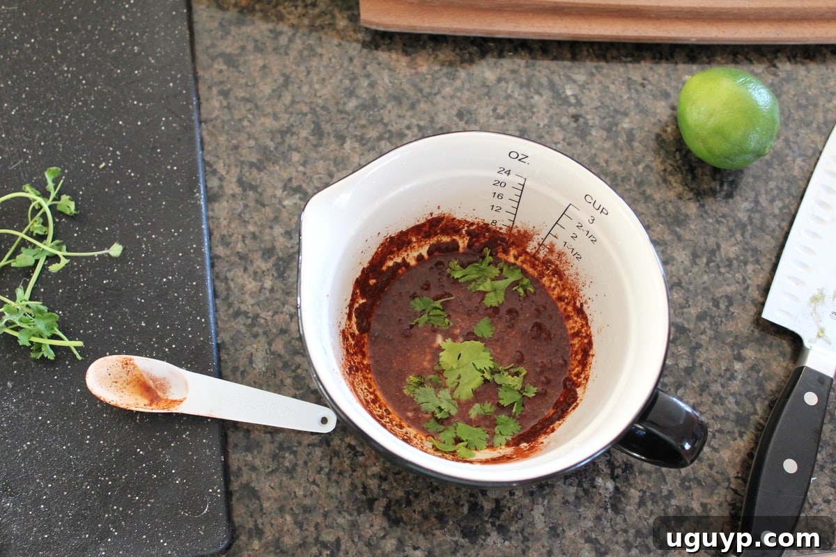 Chipotle Lime Fajita Chicken Marinade in a white measuring cup, with fresh lime halves and cilantro around it.