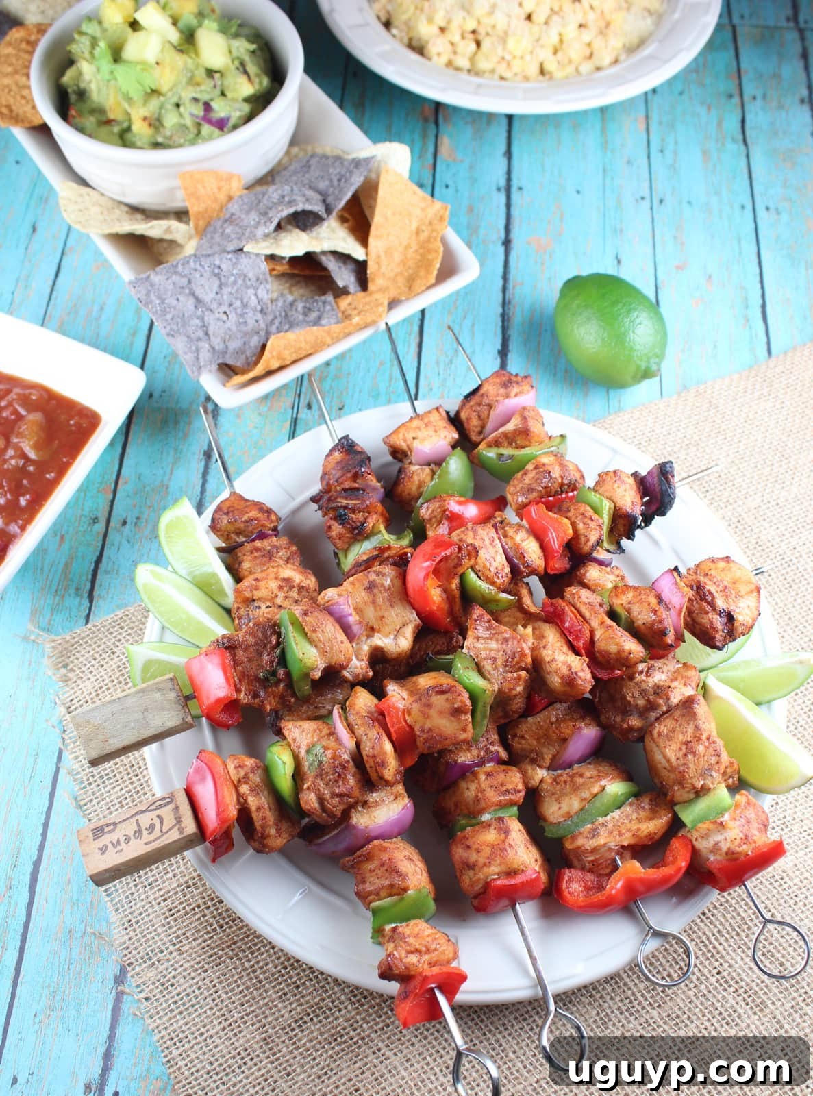 Cooked Chipotle Lime Chicken Fajita Skewers on a plate with lime wedges, accompanied by a side of tortilla chips and salsa.