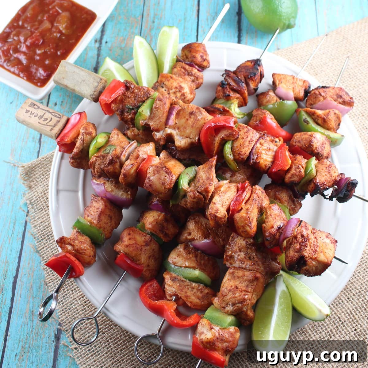 Grilled Chipotle Lime Chicken Fajita Skewers artfully arranged on a white plate, garnished with fresh cilantro and lime wedges.