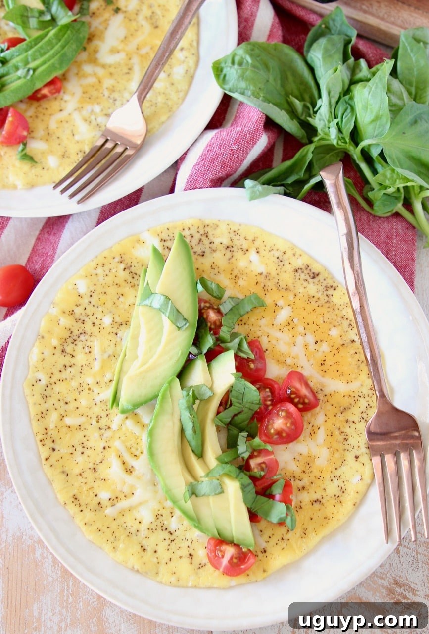 A vibrant open-faced omelette adorned with fresh avocado slices, diced red tomatoes, and fragrant basil leaves, elegantly presented on a white plate alongside a stylish copper fork.
