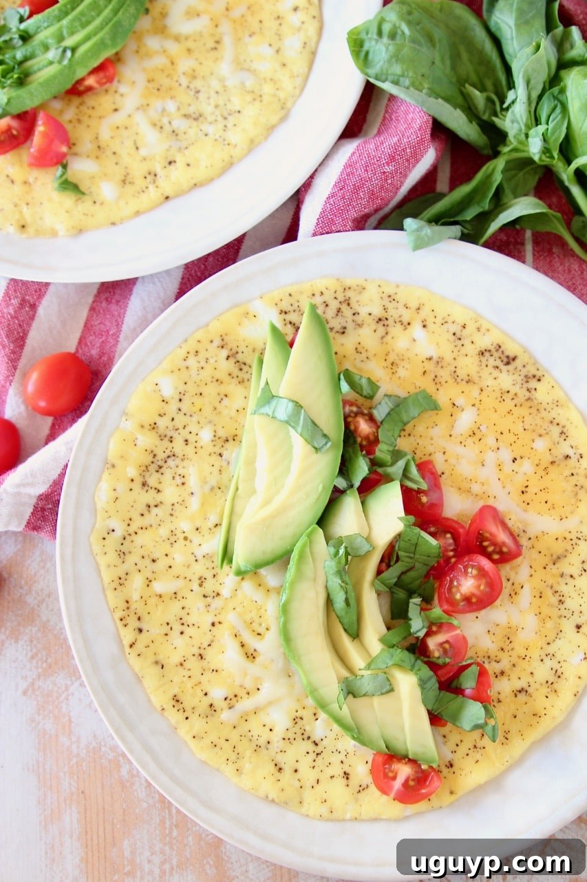 An appetizing omelette generously topped with fresh avocado slices, bright red tomatoes, and fragrant basil leaves, ready to be enjoyed.