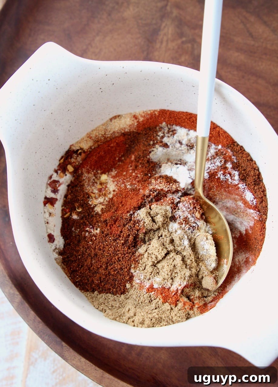 A mix of vibrant spices in a bowl with a white and gold spoon, ready for chili seasoning