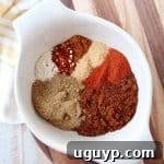 Eight spices for chili seasoning in a white bowl on a wood cutting board