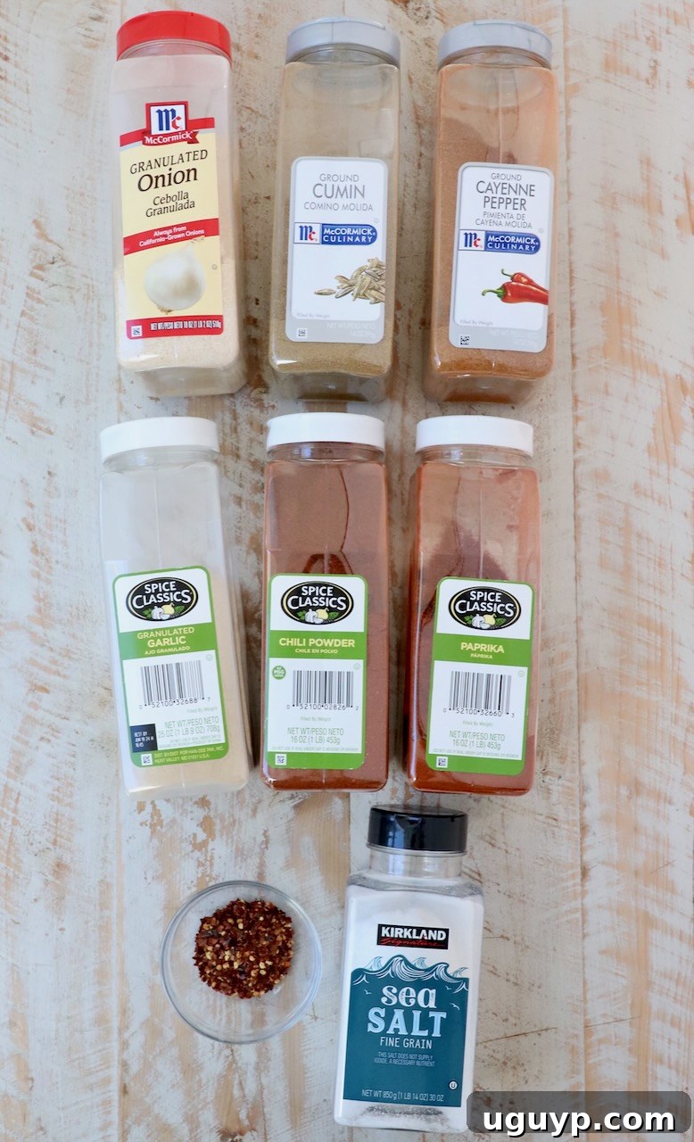Containers of assorted spices lined up neatly on a white wooden board