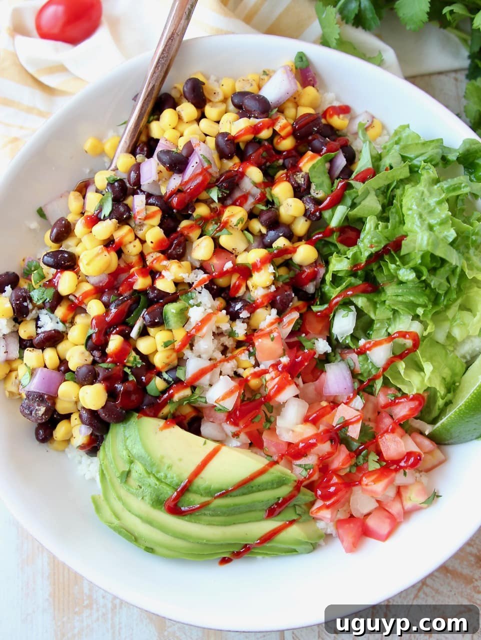 Burrito bowl with avocado, corn, tomatoes and black beans, topped with a drizzle of hot sauce in a white bowl
