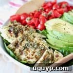Sliced pesto chicken in bowl with sliced avocado and diced cherry tomatoes