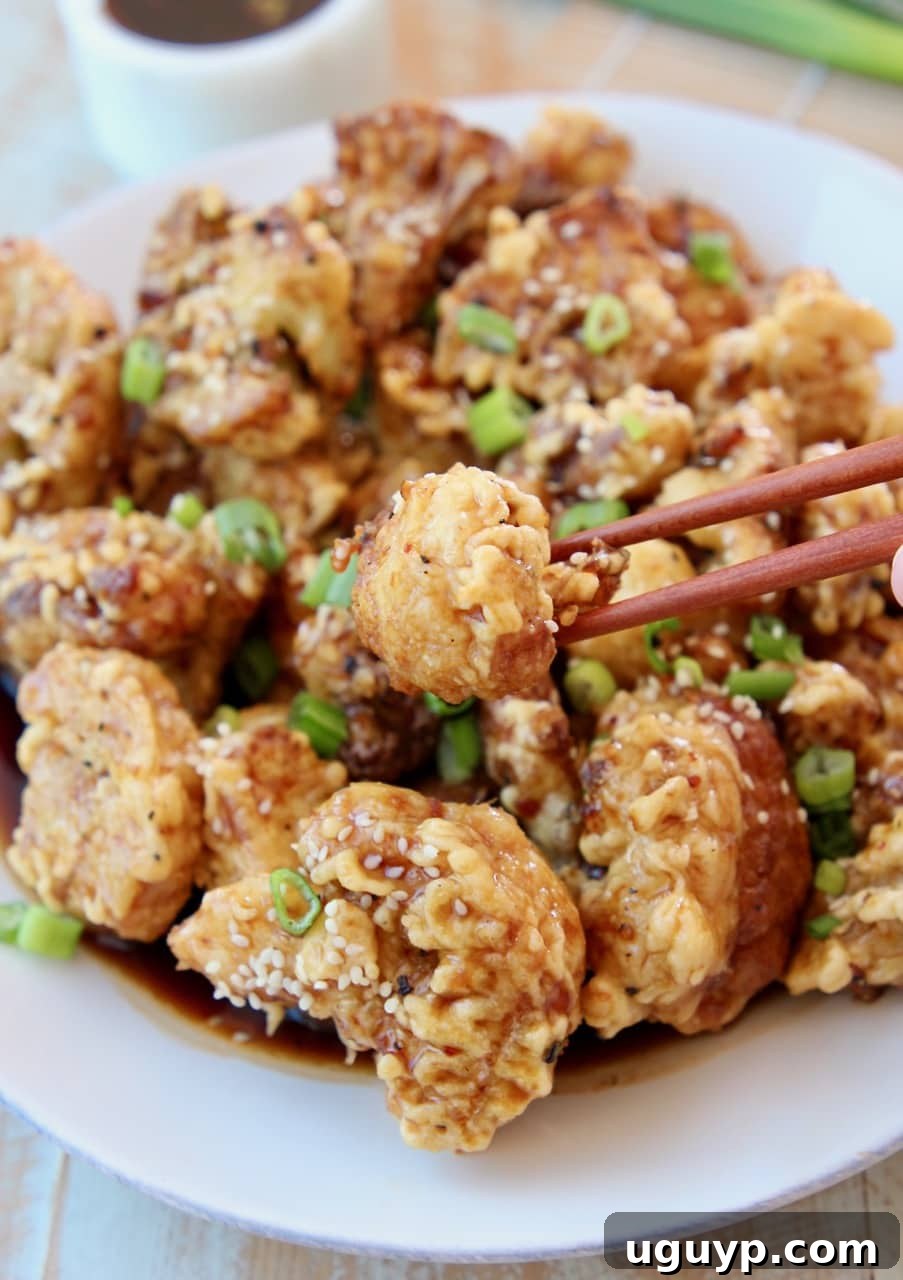 Korean fried cauliflower on plate with chopsticks picking up one piece of cauliflower