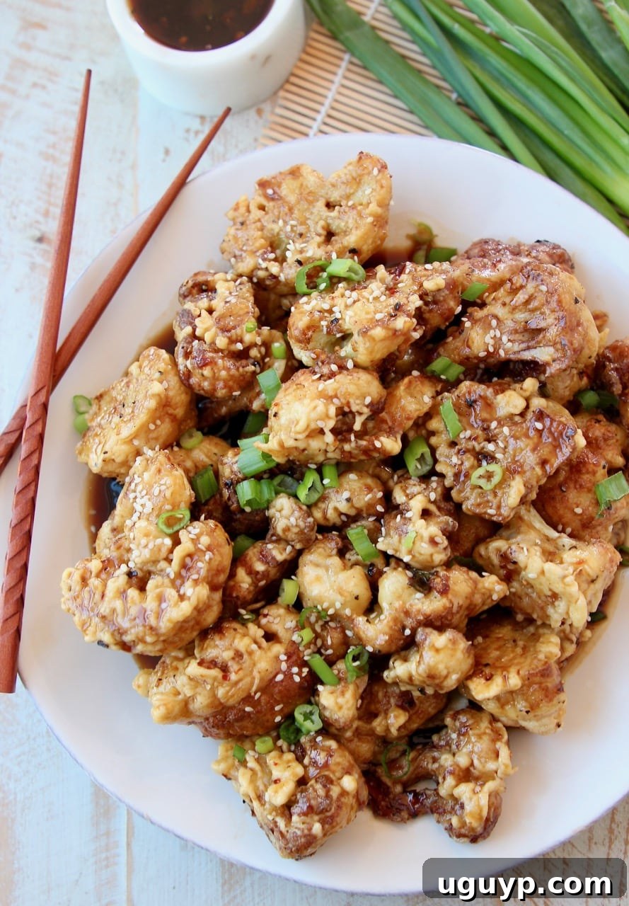 Fried Cauliflower piled up on white plate topped with Korean BBQ Sauce and diced green onions