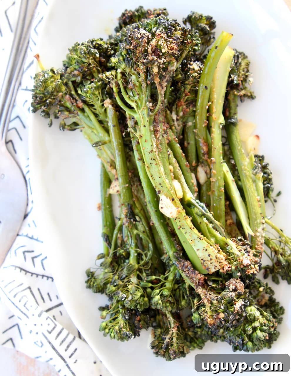 Garlic parmesan broccolini stacked up on top of each other on white plate