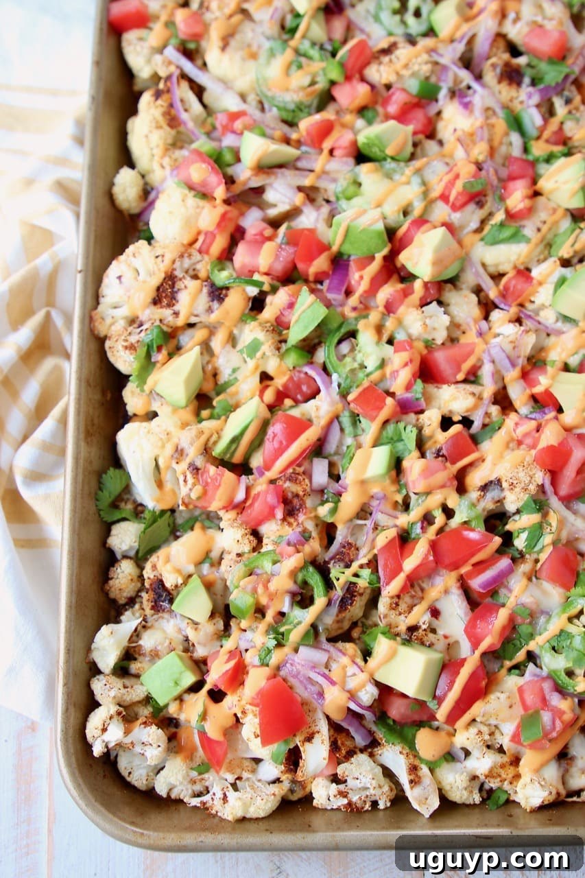 Overhead shot of cauliflower nachos on a baking sheet with chipotle cream sauce drizzled on top