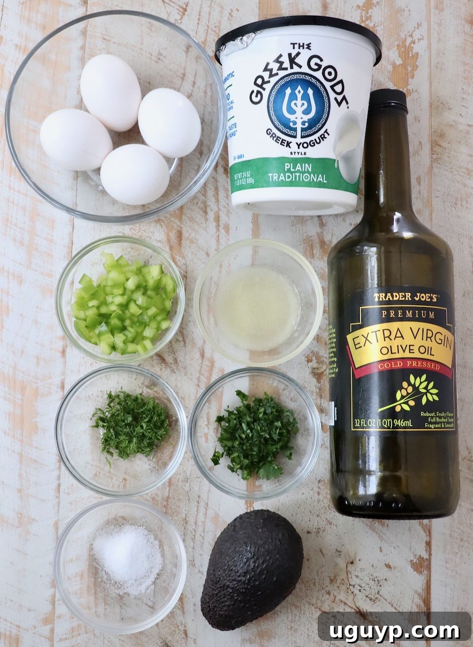 Ingredients for a creamy and healthy avocado egg salad laid out on a white wooden board, including avocados, hard-boiled eggs, bell peppers, and fresh herbs.