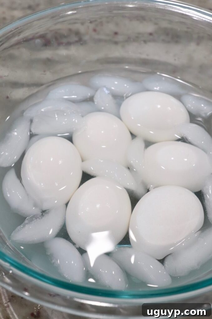 Perfectly hard-boiled eggs cooling in a glass bowl filled with ice water, an essential step for easy peeling and ideal texture.