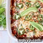 Overhead shot of enchiladas in casserole dish topped with sliced avocado and jalapenos