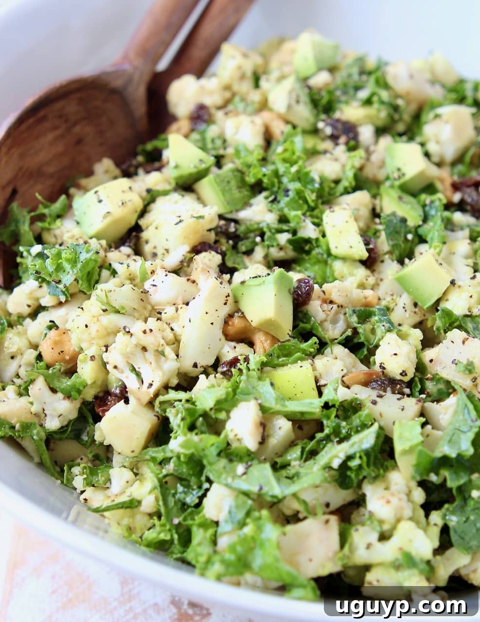 Cauliflower salad with kale, raisins and avocado in white bowl with brown wooden spoon