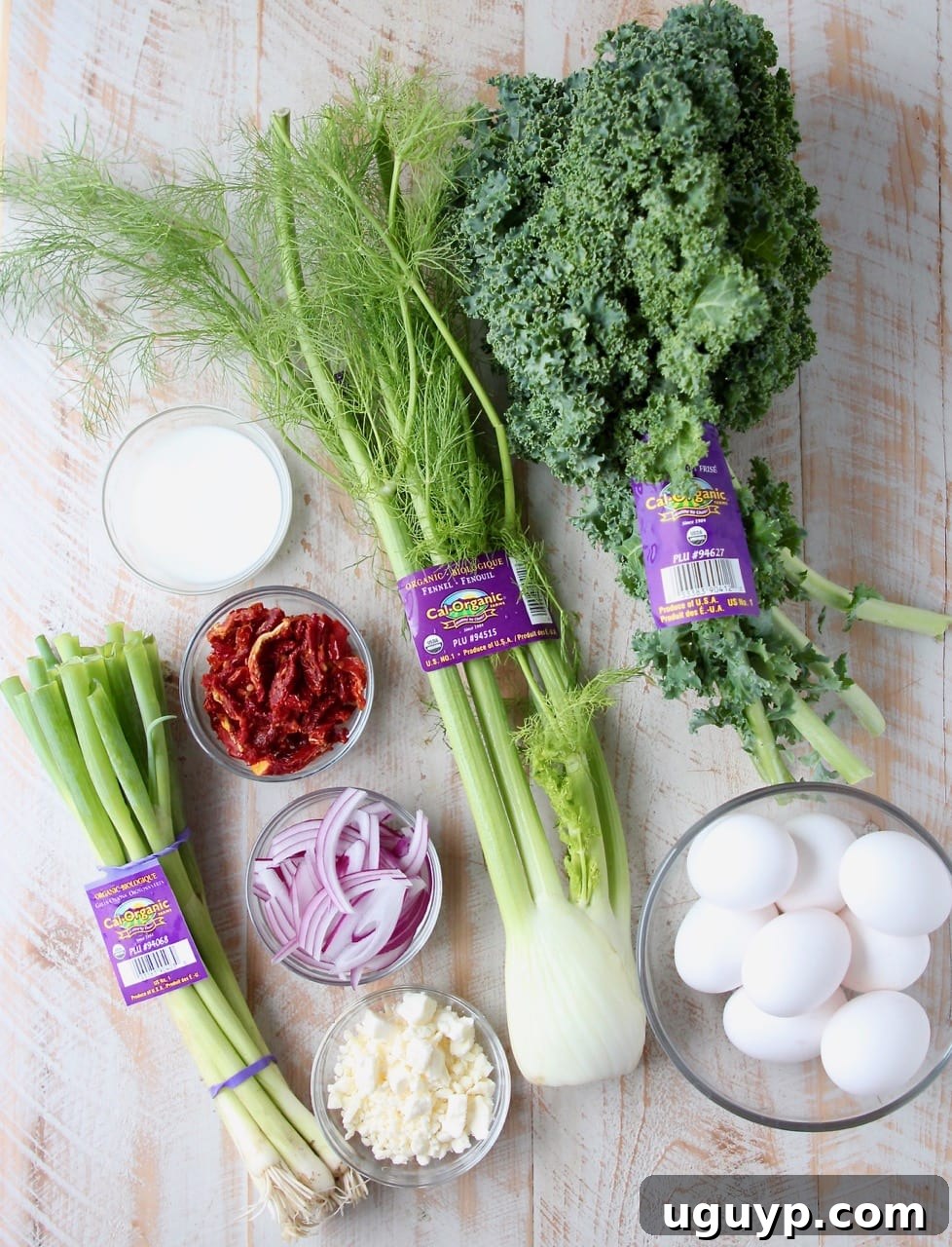 An overhead shot showcasing the fresh ingredients laid out on a wooden board, including fennel, kale, eggs, red onion, sun-dried tomatoes, and feta cheese, ready for the Mediterranean Vegetable Frittata recipe.