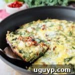 Slice of vegetable frittata being lifted out of skillet with silver spatula