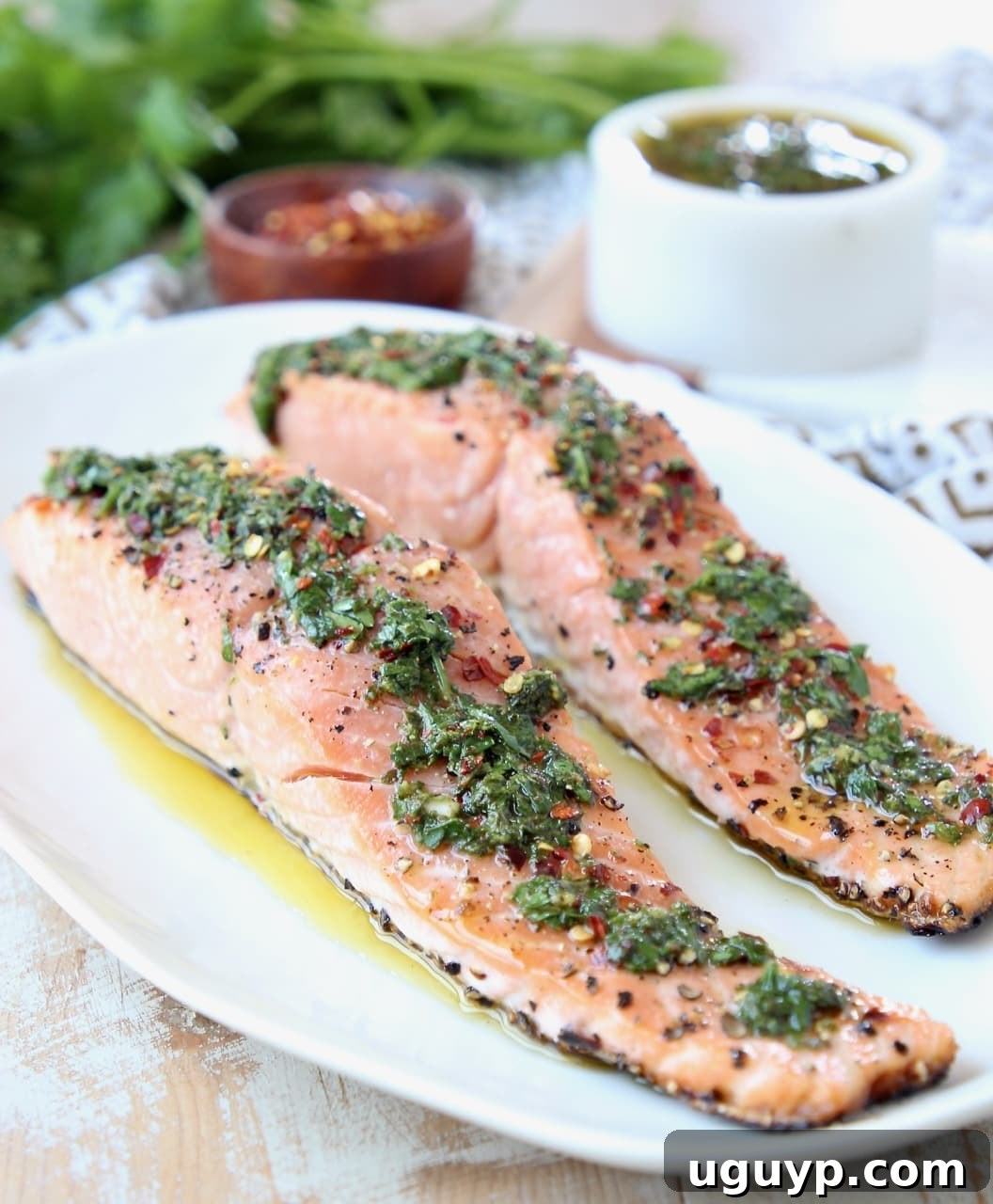 Two filets of grilled salmon on a white plate topped with chimichurri sauce