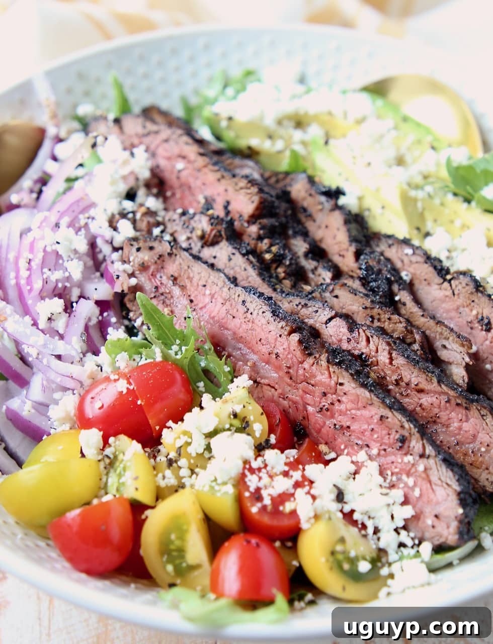 Close-up of a delicious steak salad featuring sliced coffee-crusted flank steak, cherry tomatoes, red onions, and crumbled goat cheese.