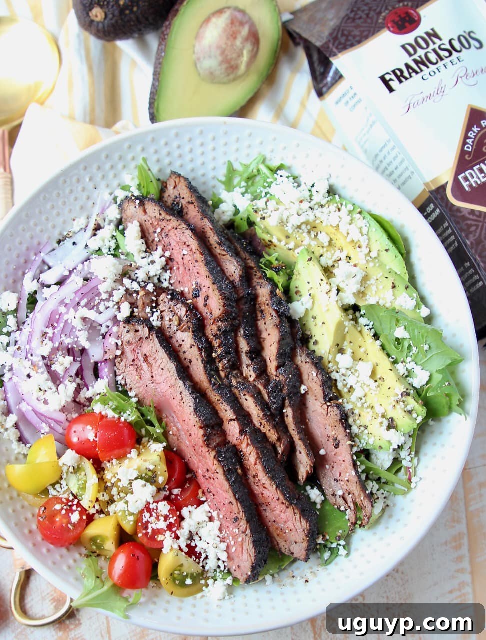 Steak salad in a white bowl with a bag of coffee beans and half an avocado on the side, emphasizing the coffee theme.