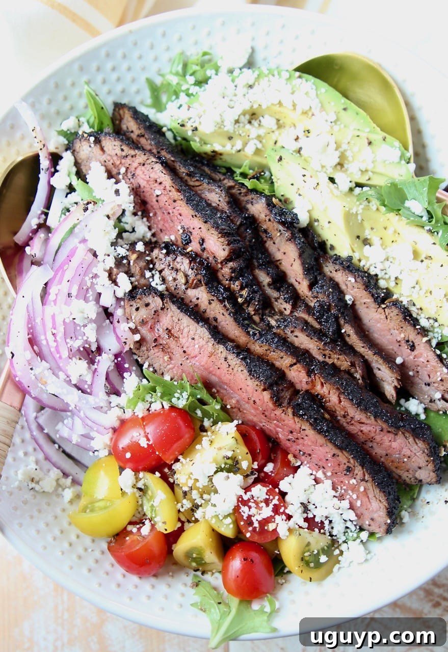 A vibrant steak salad in a bowl, featuring generous slices of steak, cherry tomatoes, avocado, and red onions.