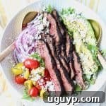 Grilled steak on top of salad in a white bowl with gold salad serving spoons