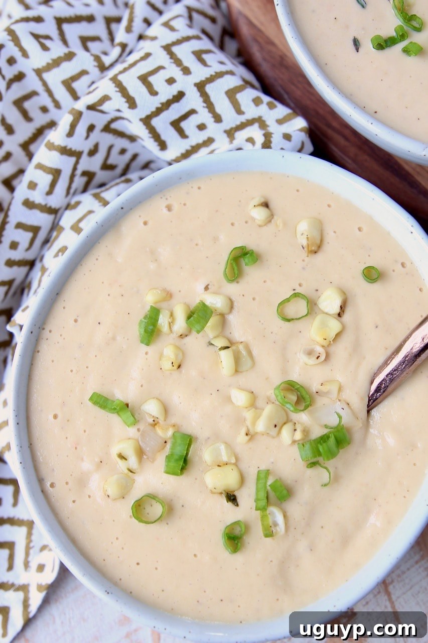 A bowl of creamy corn soup garnished with fresh corn kernels and thinly sliced green onions, ready to be enjoyed.