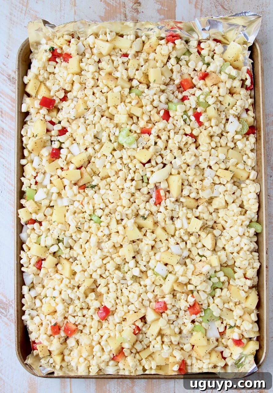 Fresh corn kernels, diced bell peppers, and chopped onions spread on a foil-lined baking sheet, ready for roasting.