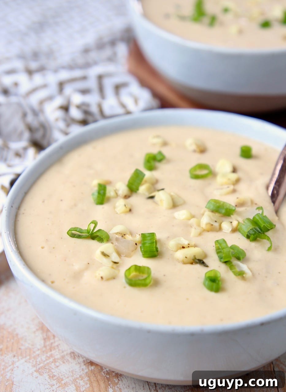 A bowl of rich, creamy sweet corn chowder, perfectly garnished, with a copper spoon resting in the bowl.