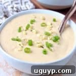 A bowl of creamy corn soup topped with fresh corn kernels and a sprinkle of diced green onions.