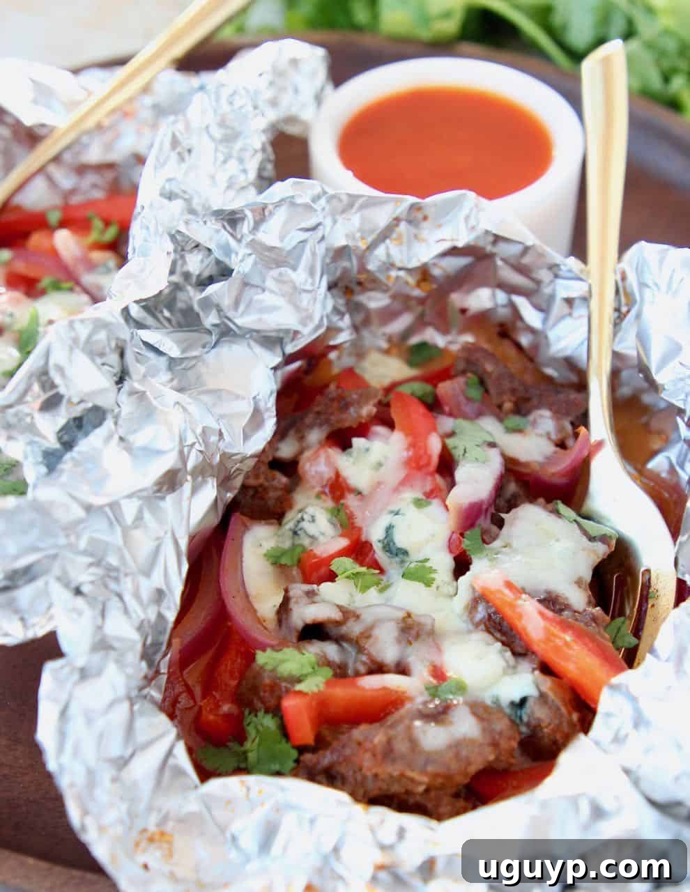 Grilled buffalo cheesesteak with juicy meat, colorful peppers, onions, and melted cheese in a foil pack, ready to serve.