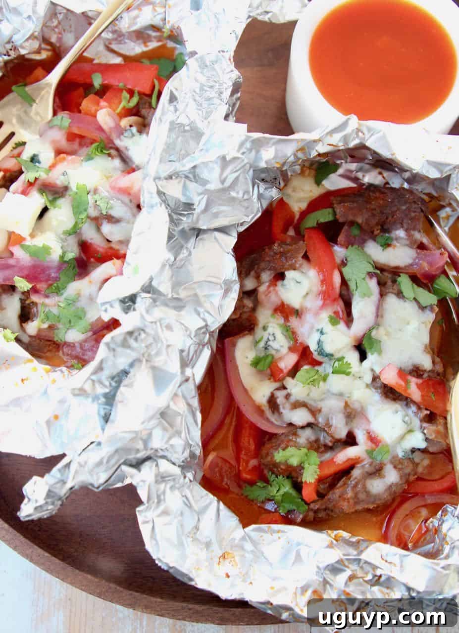 Close-up of a cooked foil pack revealing juicy steak, sautéed peppers, caramelized onions, and perfectly melted cheddar and blue cheese, ready to be enjoyed.