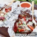 Cheesesteak foil packs with side of buffalo sauce in bowl and gold fork in foil pack