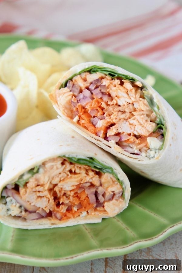 Buffalo chicken wrap, sliced in half and arranged on a green plate with a side of potato chips, showcasing a vibrant and appealing meal.