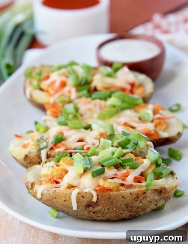 Golden-brown buffalo chicken potato skins, topped with fresh green onions, neatly arranged on a white oval plate, with a small bowl of ranch dressing in the background.