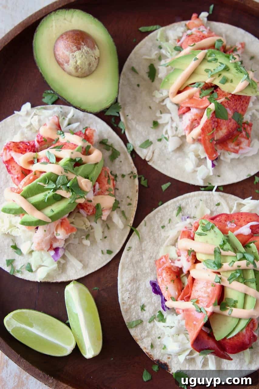 Overhead shot of two beautifully assembled lobster tacos on a wooden serving board, accompanied by lime wedges and half an avocado, emphasizing the fresh ingredients.