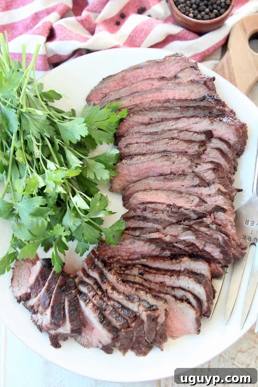 Sliced tri tip steak on white plate with fresh parsley
