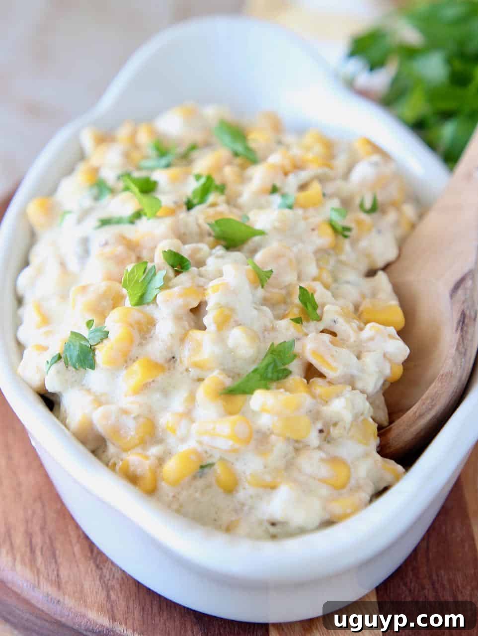 Delicious creamy crock pot creamed corn served in a decorative white dish with a wooden spoon, ready to be enjoyed as a family favorite side dish.