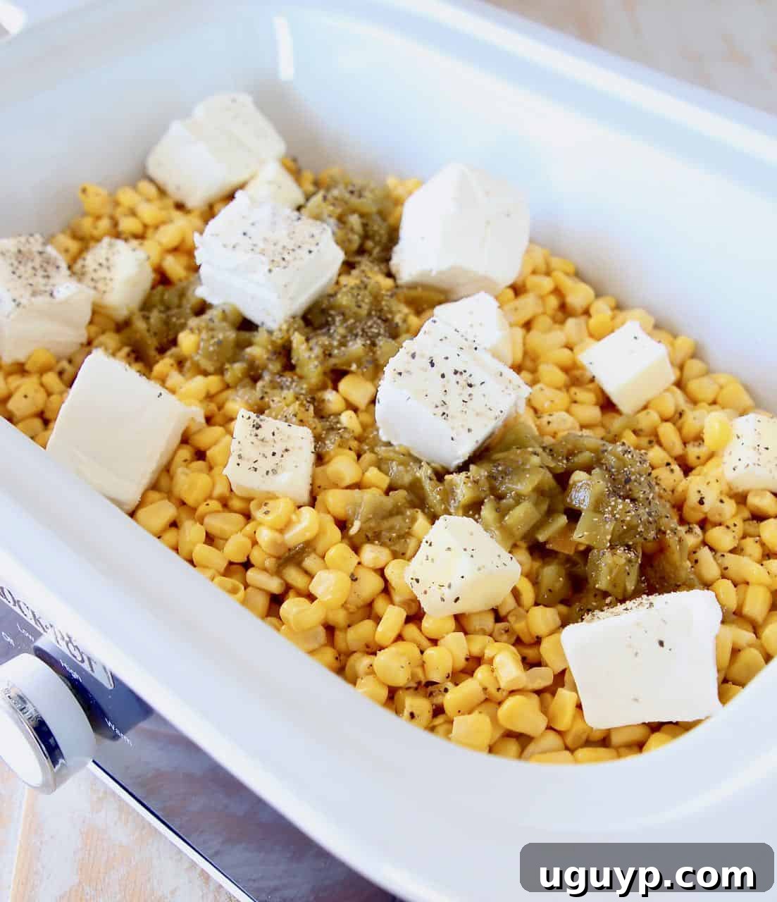 Ingredients for crock pot creamed corn in a slow cooker before cooking, showing corn, butter, cream cheese, and green chilies.