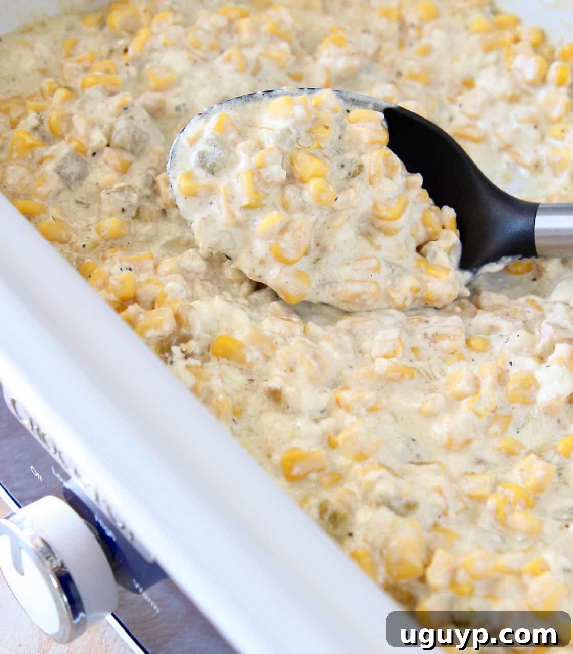 Creamed corn served in a slow cooker with a serving spoon, highlighting its readiness for a potluck or holiday meal.