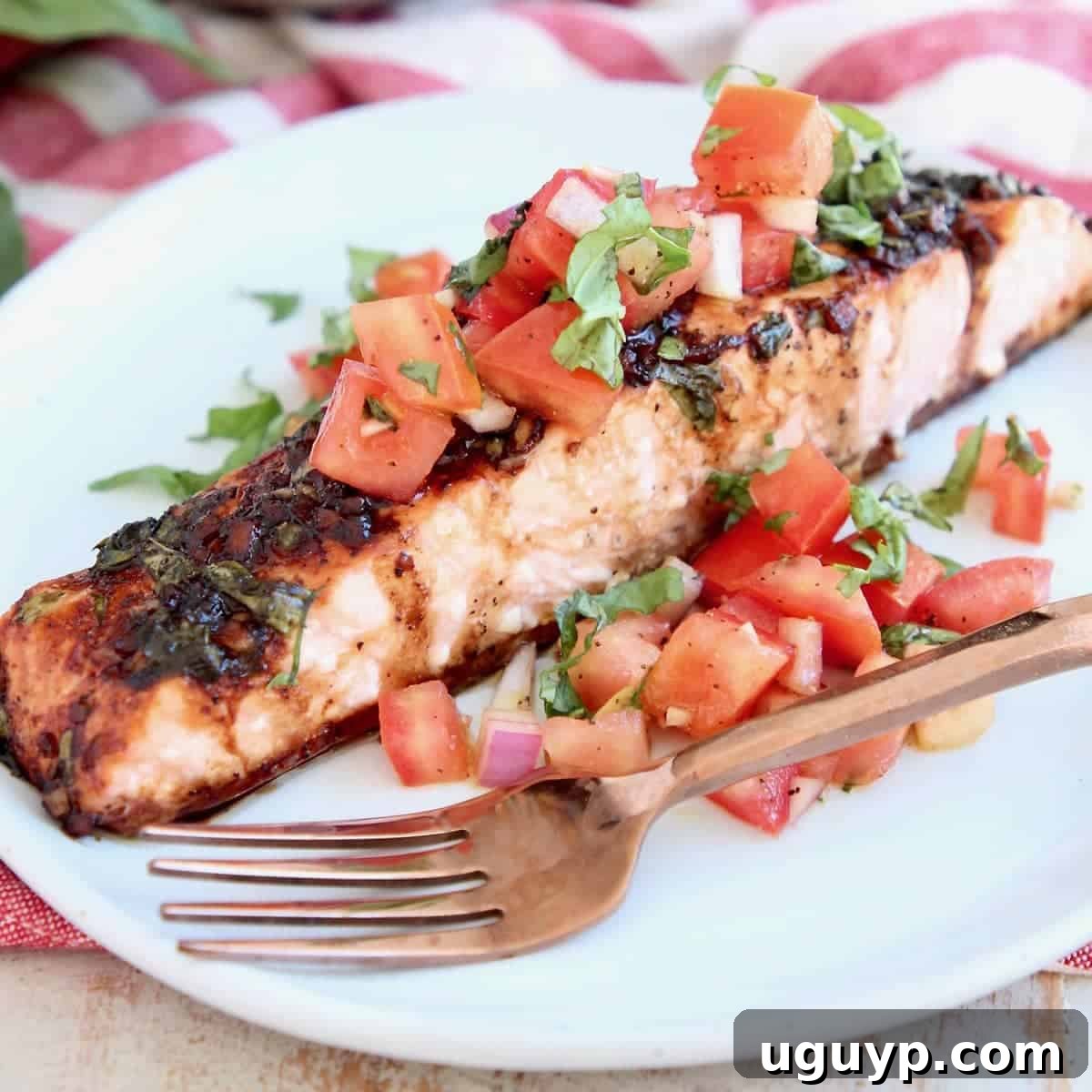 Piece of bruschetta salmon on plate with copper fork. This delicious Balsamic Baked Salmon is topped with fresh tomato basil bruschetta, offering a healthy, gluten-free, low-carb, and Whole30 compliant meal ready in just 29 minutes.